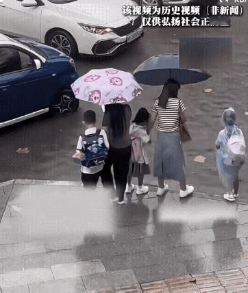 两位妈妈放学接孩子回家，路面积水严重，深过脚踝，一位妈妈背起儿子小心翼翼地走，另