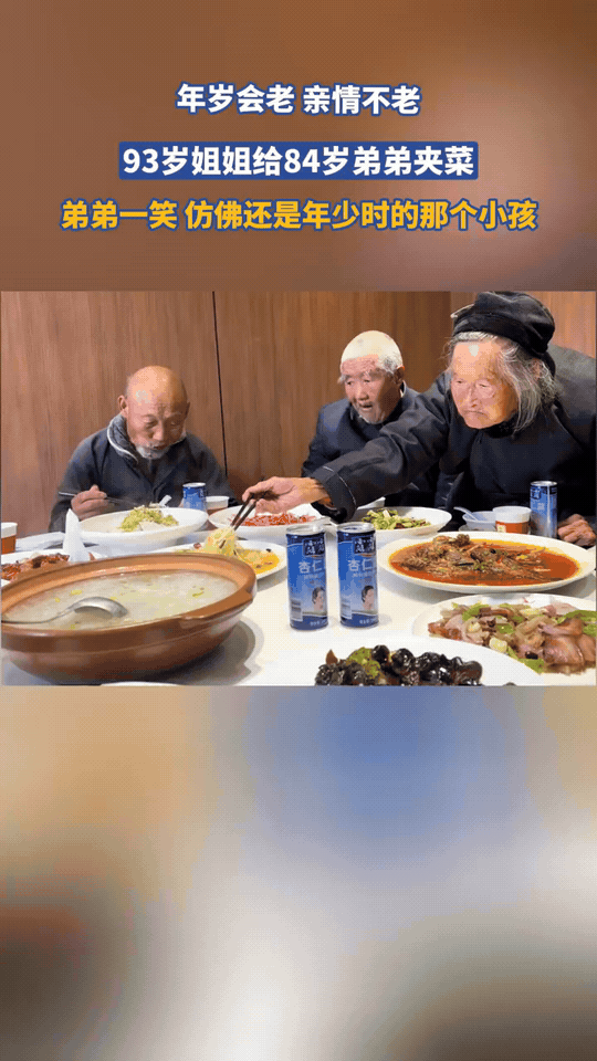 93岁的姐姐坐在餐桌旁，颤巍巍拿起筷子，夹起一筷子面条，递到84岁弟弟的碗前。