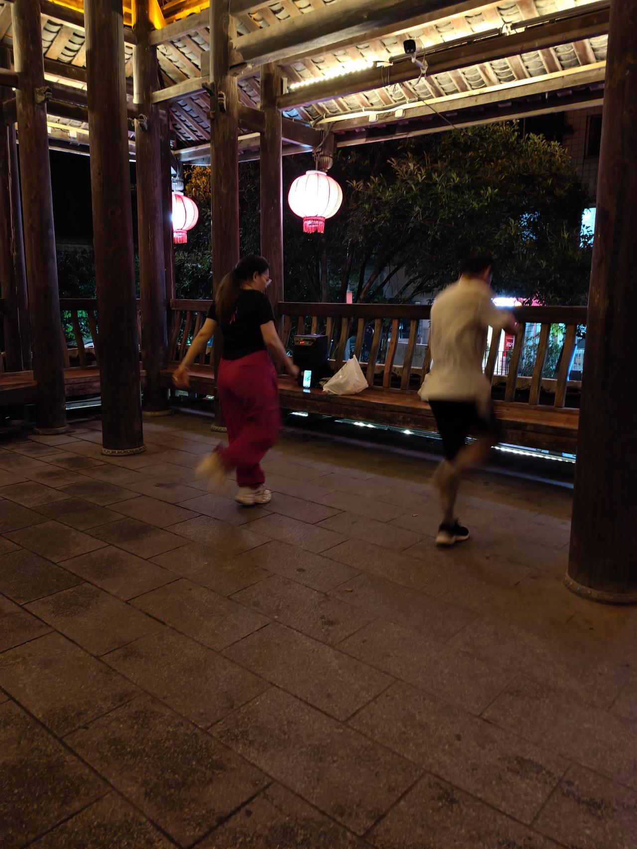 古廊夜舞
 
夜色笼罩木质长廊，红灯笼垂挂檐角，暖光缓缓洒落，古朴木柱与石板路衬