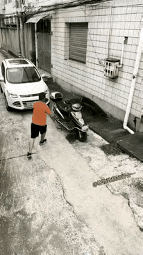 红衣男子一脚踹倒戴头盔男子停在自家门口摩托车，然后大摇大摆的就要去开车走人，没想