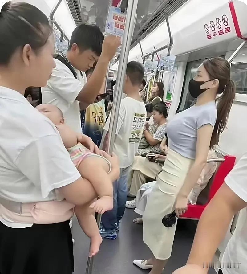 在拥挤的地铁车厢里，一位面容疲惫的女人，正抱 着婴儿艰难地站着。那婴儿在怀中不安