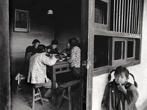 照片上一家人围桌吃饭，门外一个小女孩儿依在窗户下，一个手指头放在嘴唇上，那是想吃