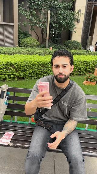 一名外国男子手上拿着大把的现金人民币坐在街头炫耀？
他这是在炫富吗？
其实外国人