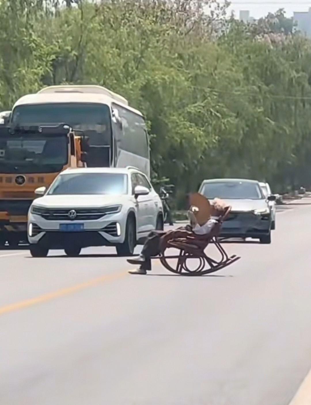 4月26日，陕西咸阳国道上一位大爷把躺椅摆在公路中间，躺下翘着二郎腿、摇着蒲扇晒