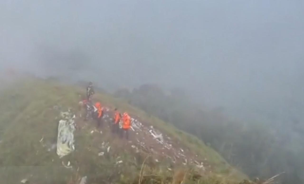 在雾气弥漫的山野间，救援人员身着橙色救援服，正艰难地在陡峭的山脊上推进。山坡上散