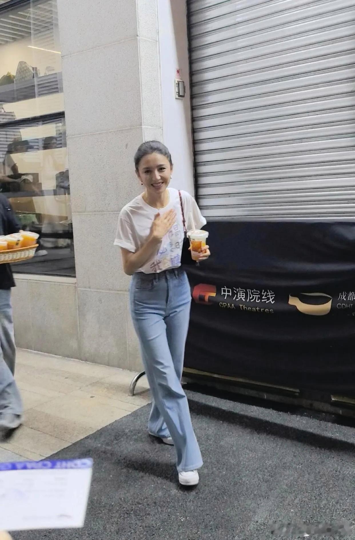 佟丽娅下班路透释出，白T恤搭配浅蓝喇叭牛仔裤，穿搭简约清爽。手持饮品笑容和煦，褪