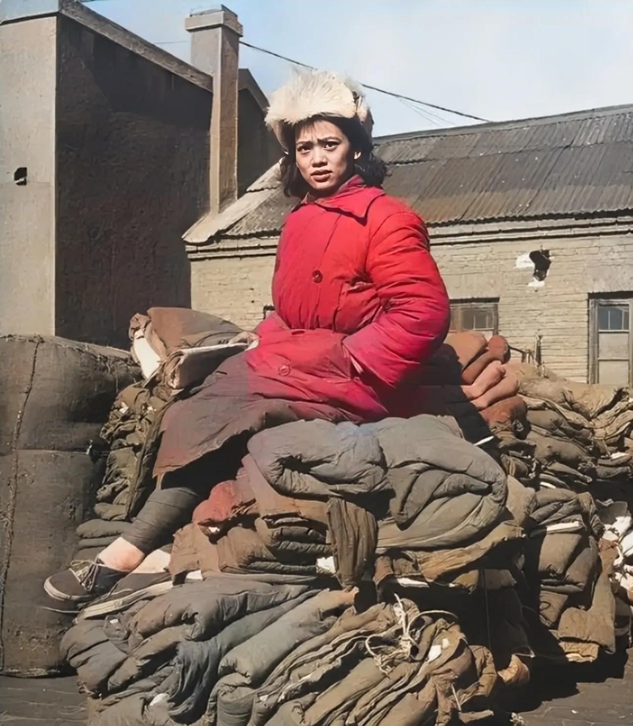 1948年，淮海战役期间，一名国民党女兵，神情呆滞，双手插兜，坐在成堆的棉服上四