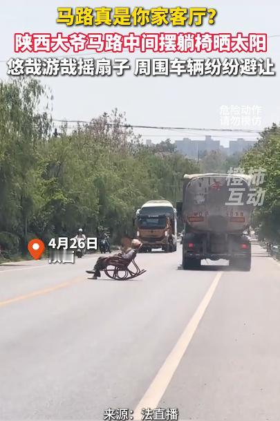 大爷躺马路中间晒太阳 车辆纷纷避让，看到视频里大爷悠哉地摇着扇子躺坐在摇椅上晒太