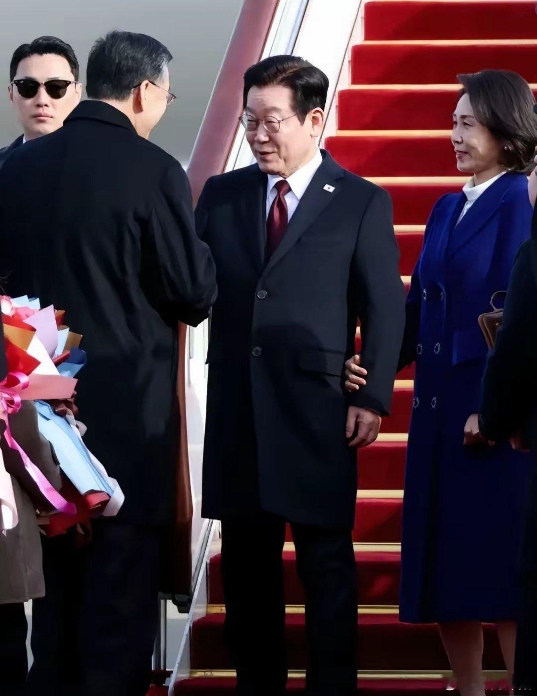 韩国总统李在明偕夫人金惠景及随行团队，一同现身机场。现年61岁的李在明，身着长款