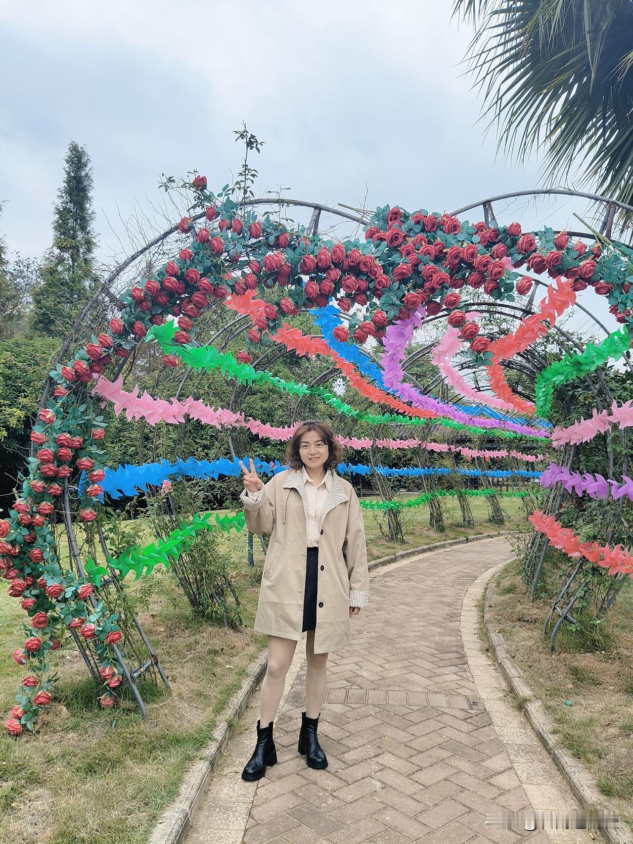 小径向绿意里蜿蜒，花艺拱廊先撞入视线——艳红玫瑰攀满支架，彩风车在拱间叠成流动的