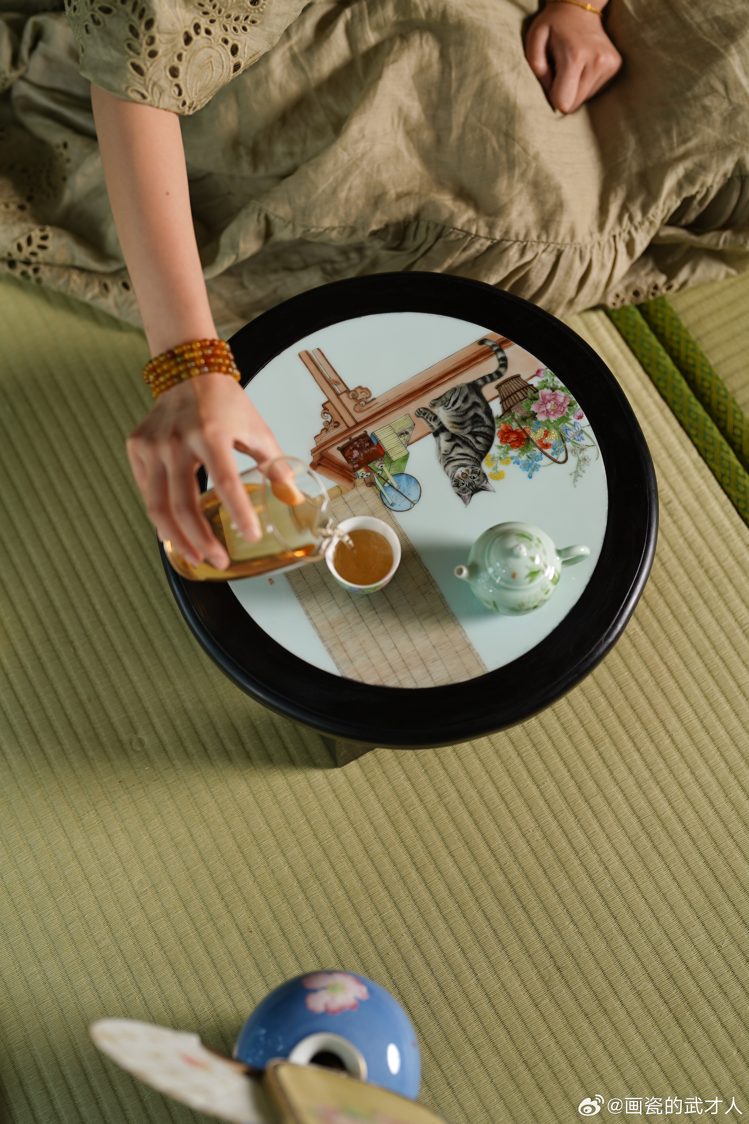 一张小圆茶桌，画了只猫咪和清供，用胡桃木镶嵌。其中最考验画工的不是猫咪的一根根丝
