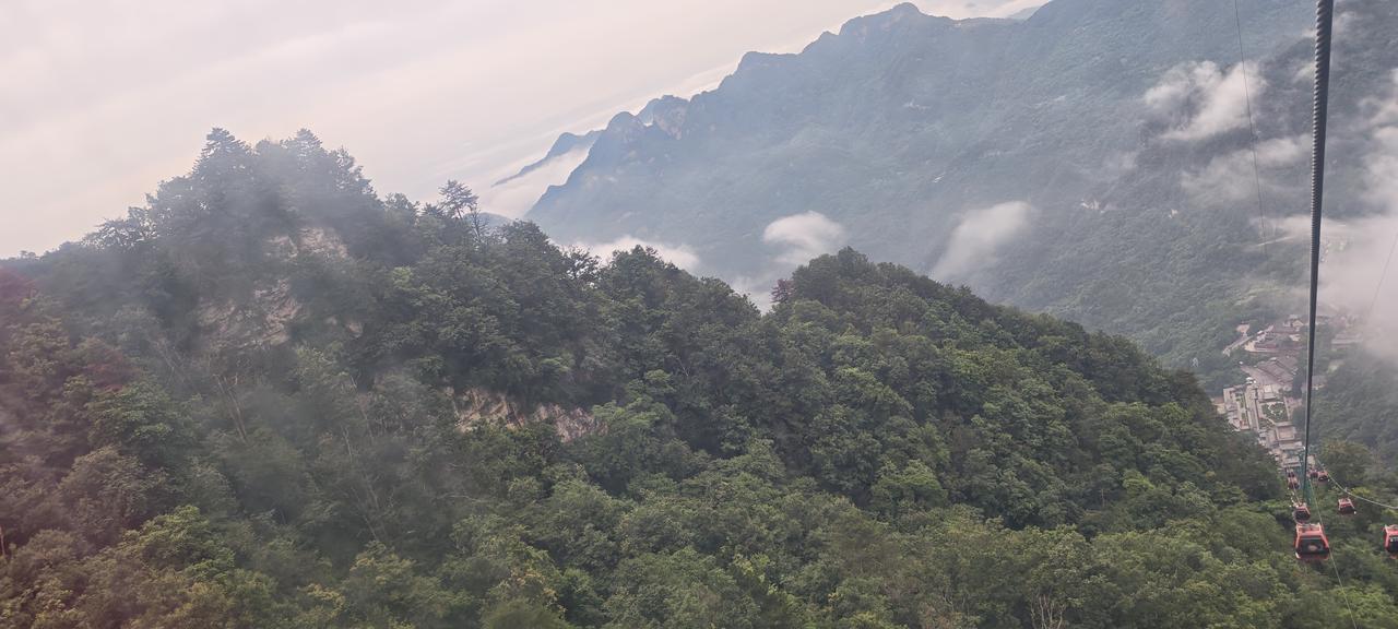 这是在武当山的缆车上拍的，钢索斜切入画，远山层叠如墨，云雾从谷底翻涌上来，。雾不