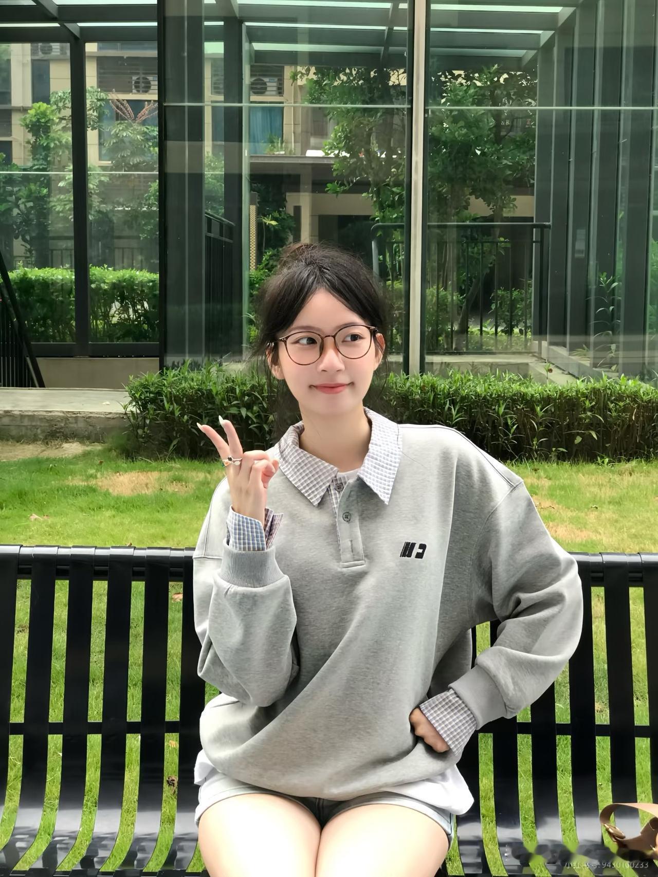女孩坐在长椅上，比出V字手势。