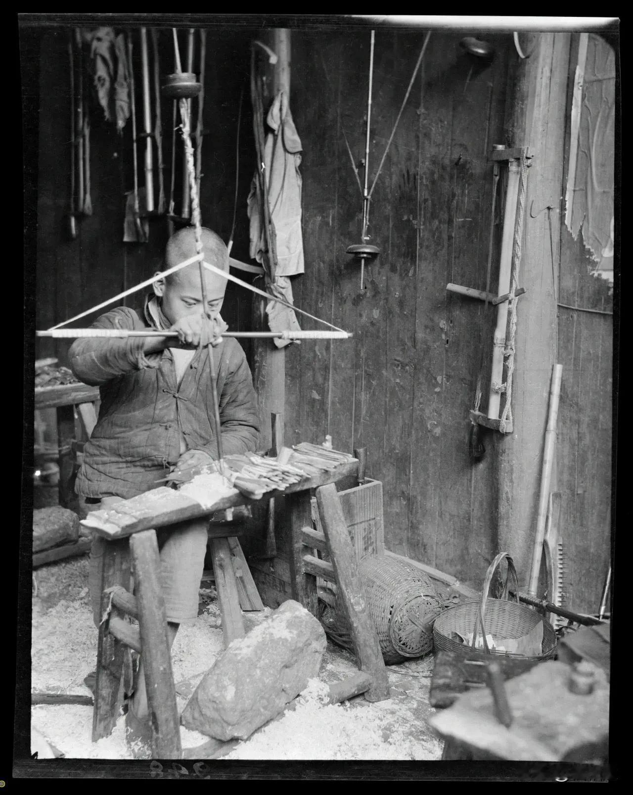 拍摄于1915年的老照片，一个10几岁的男孩在木工店里工作。他坐在一张木制的工作
