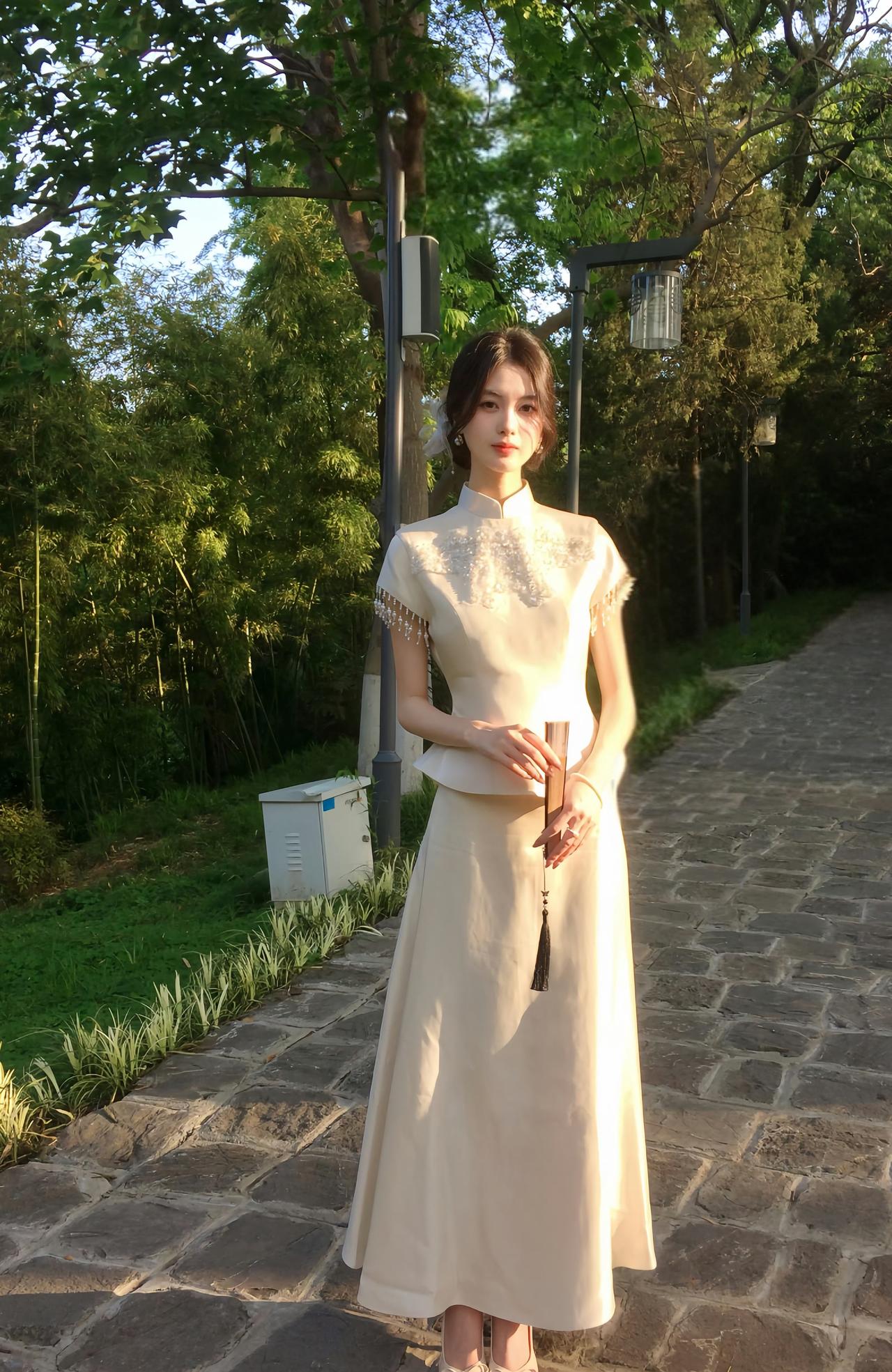 一身米白色中式套装，上衣有精致刺绣和流苏装饰，搭配同色系长裙，手持带流苏的物件，