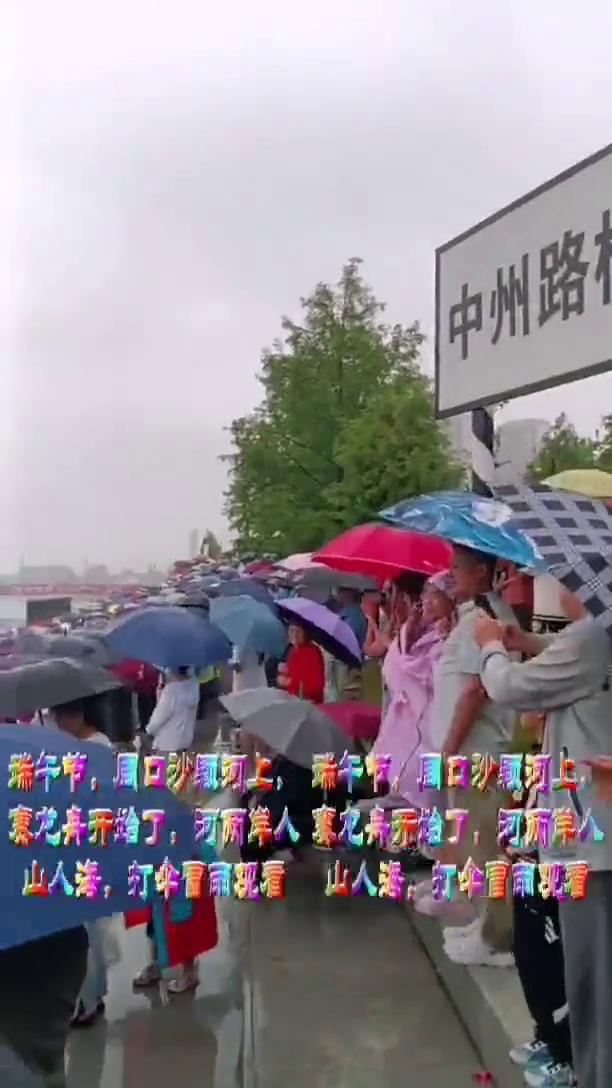 科，瑞午节，周口沙颗河上影科寒龙弃开始了，河两岸人认深了聘山人海，打伞冒雨观看。