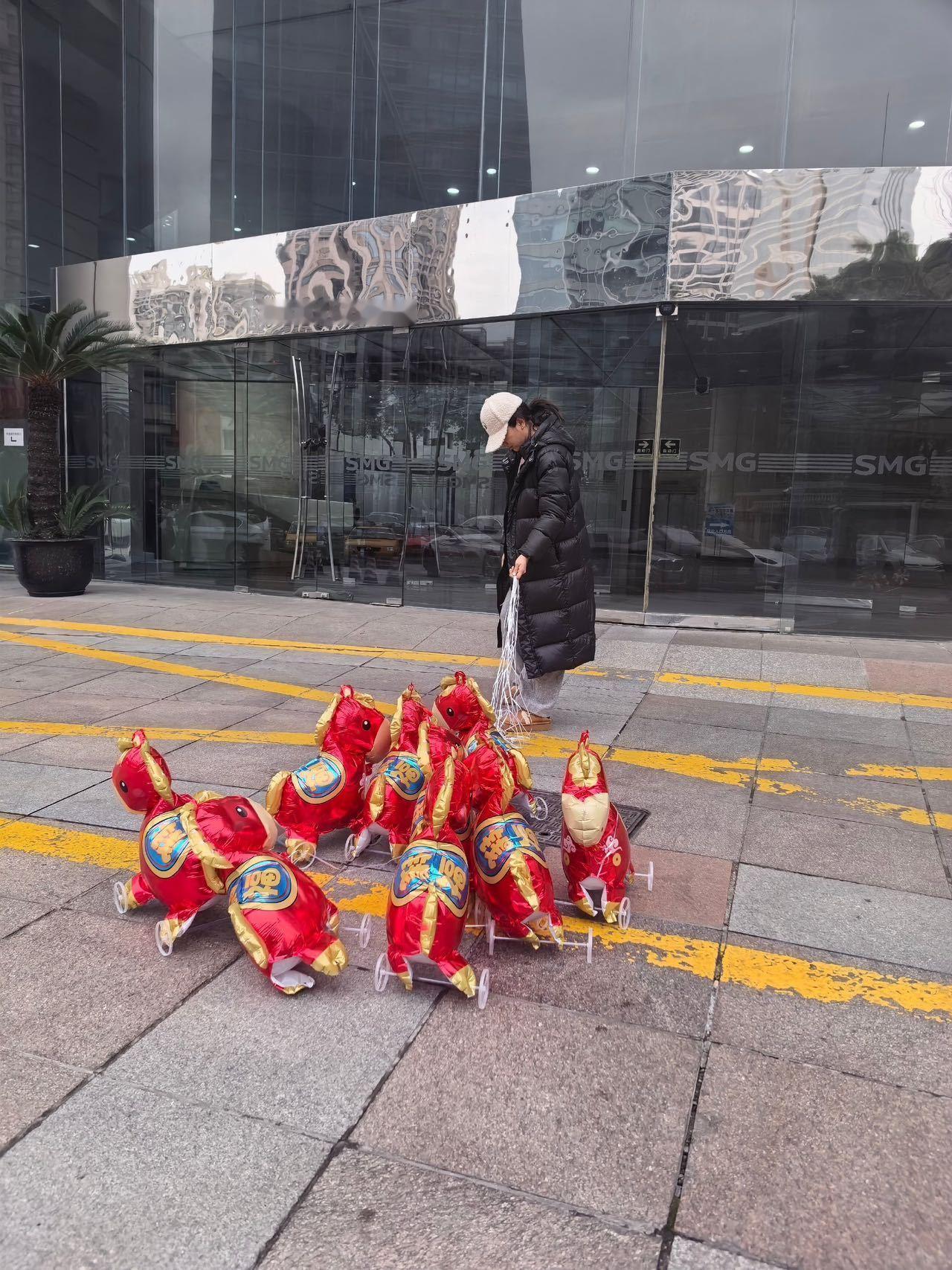 黄奕牵着9匹气球马上班 黄奕这波春晚上班路透太有趣了！身后9匹印着祝福语的气球马