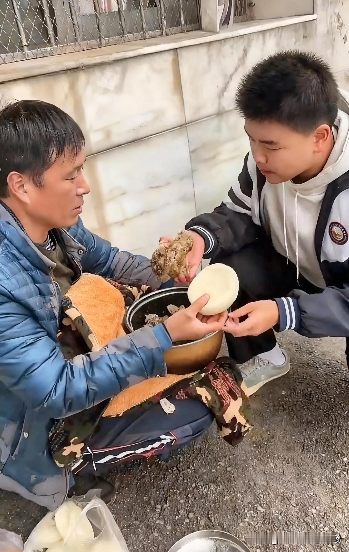 男子穿着一件破旧掉皮的棉袄蹲在学校门口旁边，而且怀里还用挡风被紧紧裹着一个锅，打
