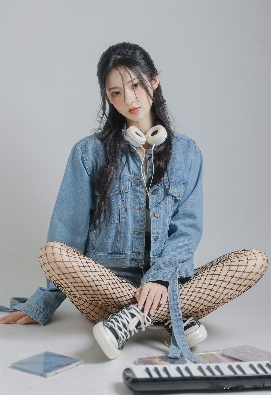 一个女孩坐在地上，戴着耳机，穿着牛仔外套和渔网袜。
