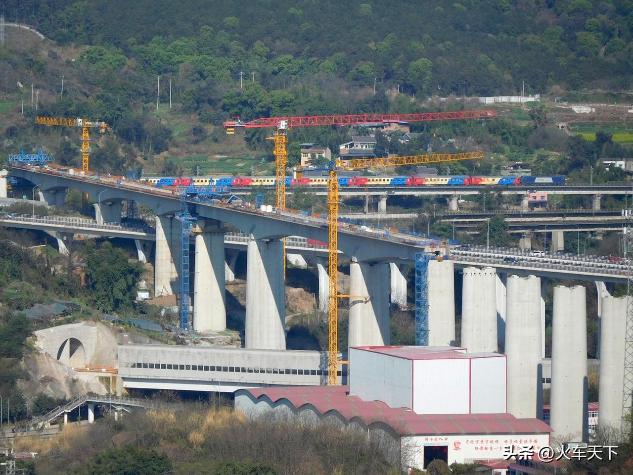 一列特色涂装的旅游列车经过远处的铁路桥，近处施工中的是成渝中线高铁，很明显的坡道