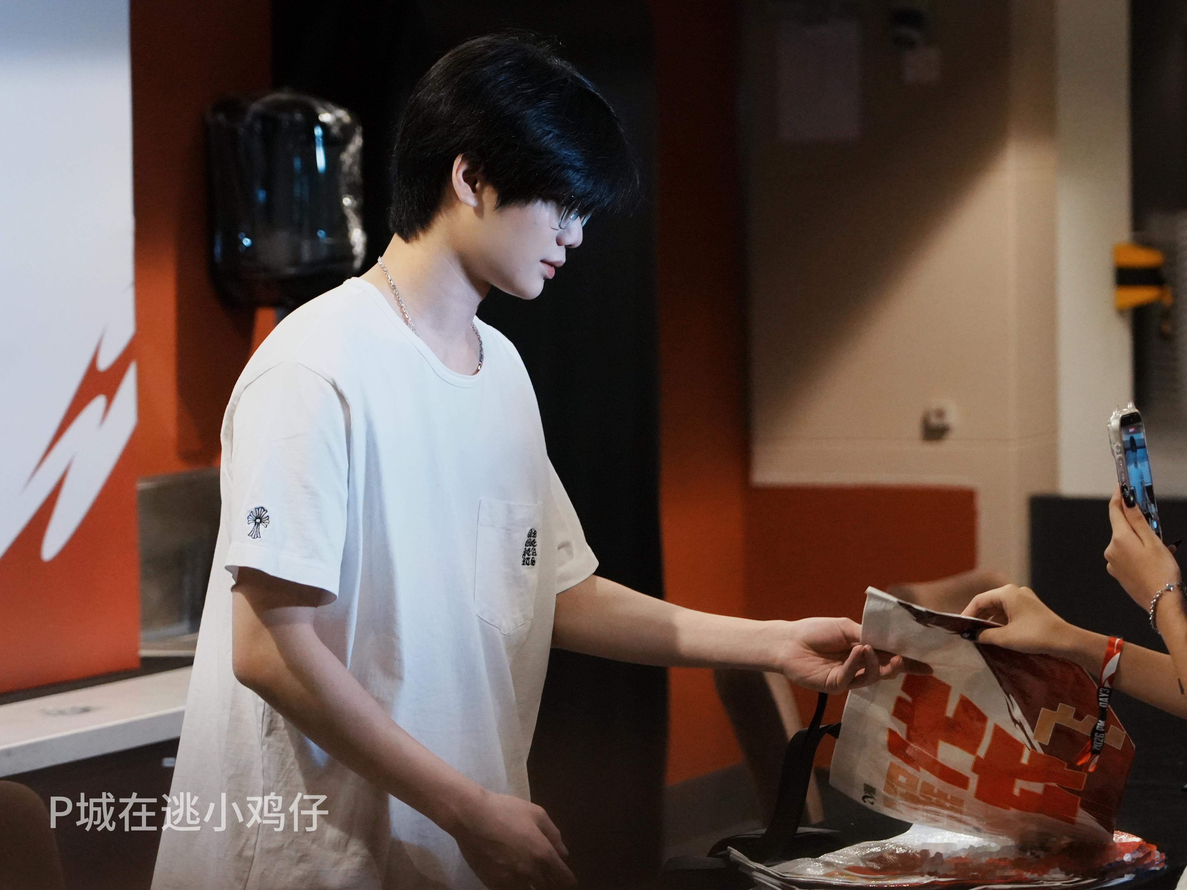 澳门邀请赛总决赛现场返图。该选手身着白色T恤佩戴眼镜，发型整齐顺滑，正在现场与粉