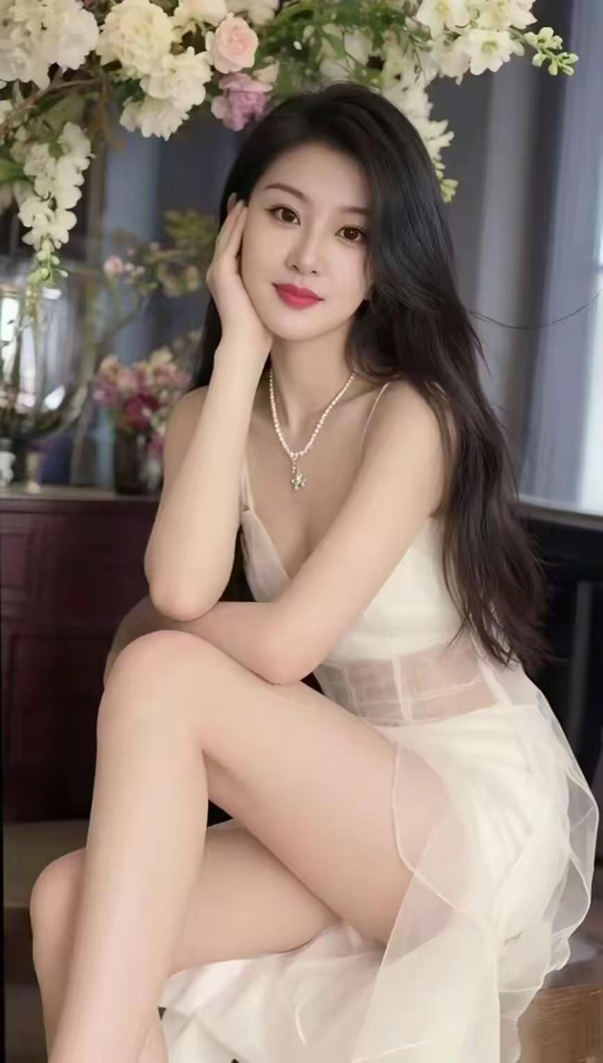 一个穿白裙子的美女在花前摆姿势。