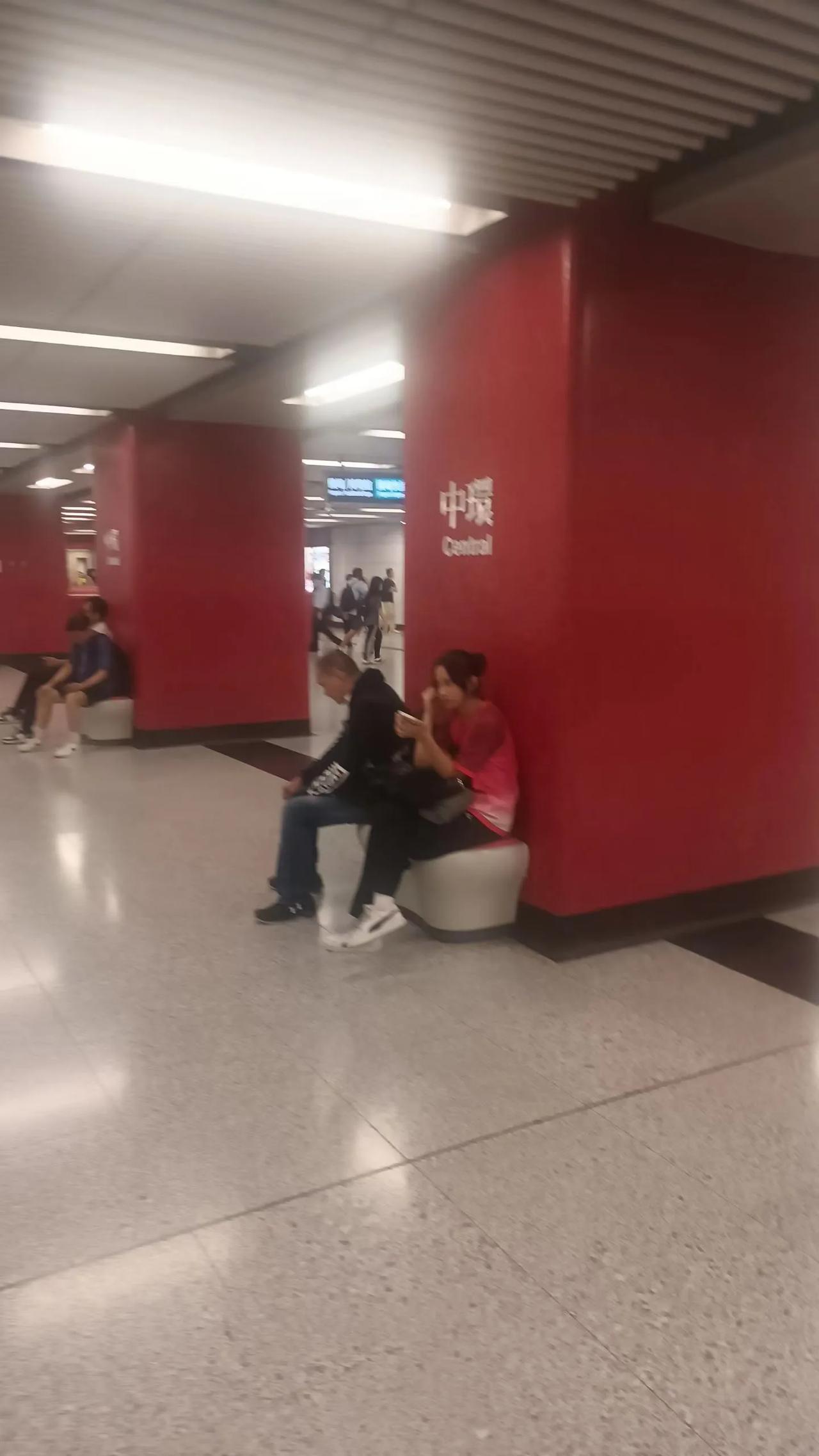 人流如鲫整洁明亮是地铁港岛中环站的场景，宽敞大堂倚墙设立的坐凳，有需要的小憩片刻