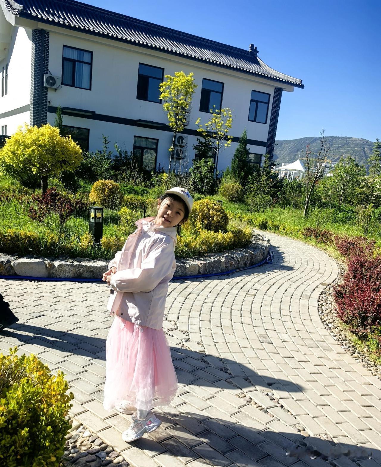阳光正好，微风不燥。
小姑娘穿着粉外套、白纱裙，
在开满嫩黄小灌木的院子里，
留