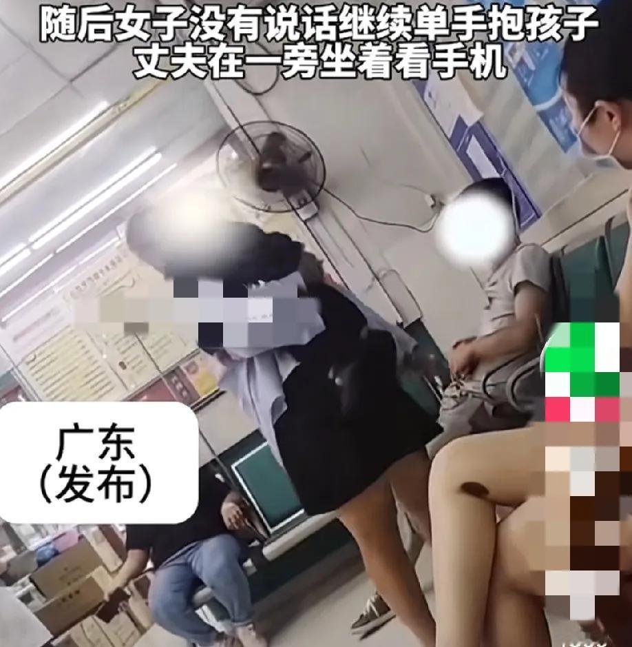 一位女子在医院给孩子打吊瓶，一边吊着一边单手抱着孩子，另一只手拿着手机。
这时她