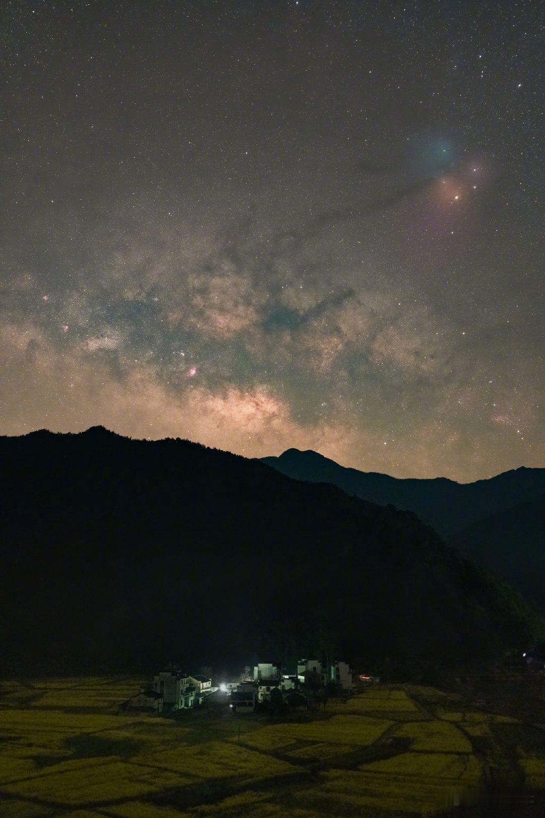 山脊以南，古村的灯火在夜里静静燃着，像落入山间的几粒余烬。银河从山头漫开，将浩瀚