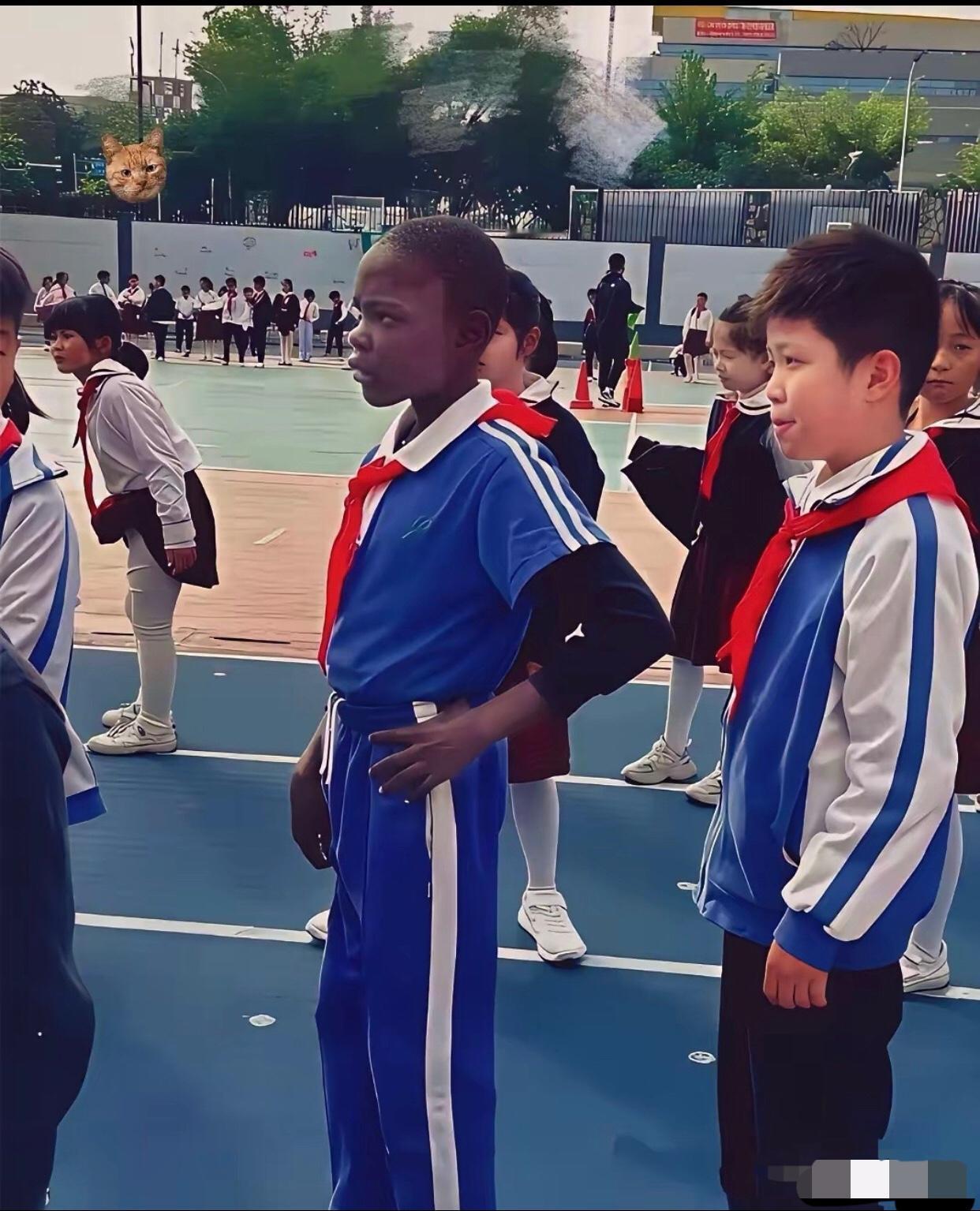 某小学校园，一名黑人小学生站在一群中国小学生中间，他的胸前佩戴着鲜艳的红领巾，他