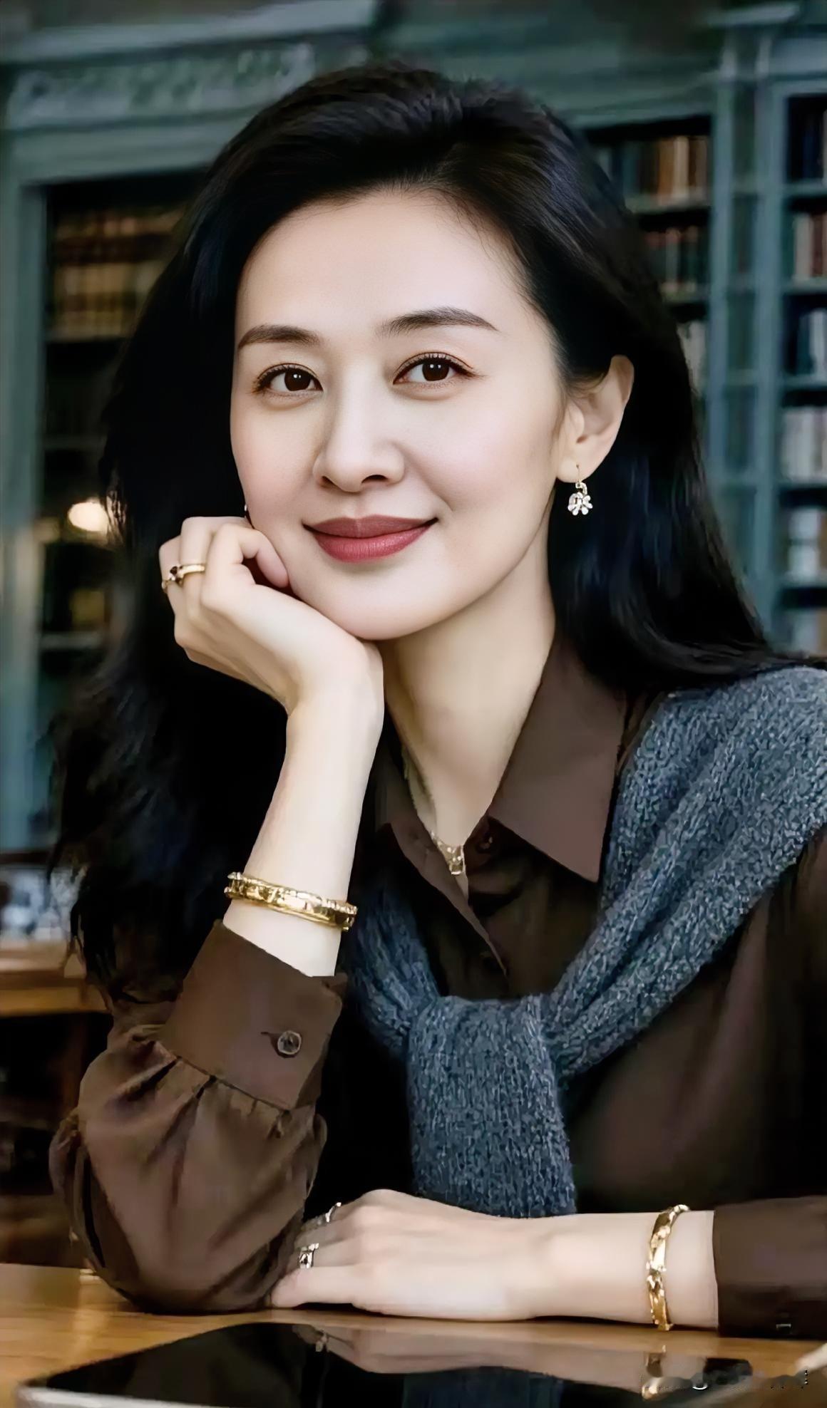 墨发垂落肩头，

棕衫裹着温柔。

金镯轻吻腕间，

指尖托腮如诗。

书墙静默