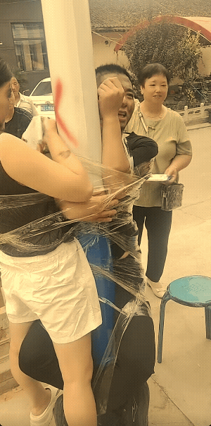 这不是新郎和新娘。
发视频的人说，这是家里生了女孩过百宴，绑在电线杆子上的俩人，