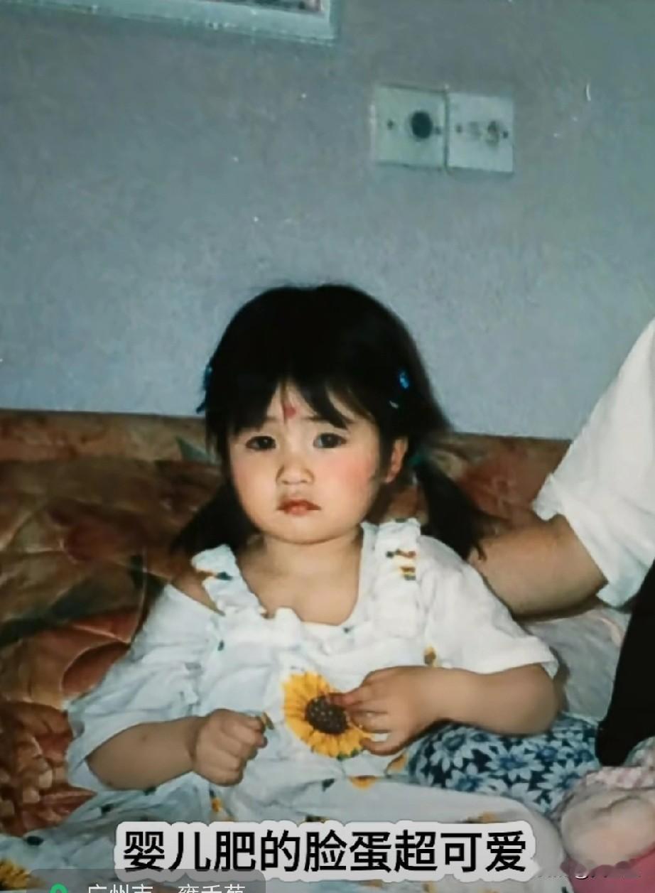 快来看，这张90年代末的生活照！小女孩坐在沙发上，手里捏着向日葵装饰，婴儿肥的脸