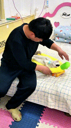 这位小哥坐在床边，细心照料着怀里的小奶猫。小猫安稳躺在香蕉造型小窝里，乖乖仰着身