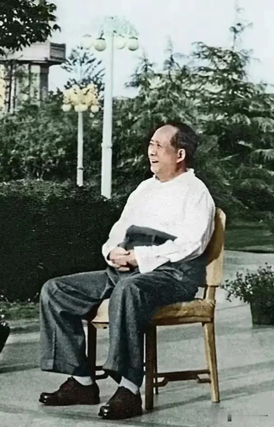 毛主席安然坐于木椅，转头含笑望向一旁。褪去繁忙公务，神态松弛随和，质朴日常模样尽