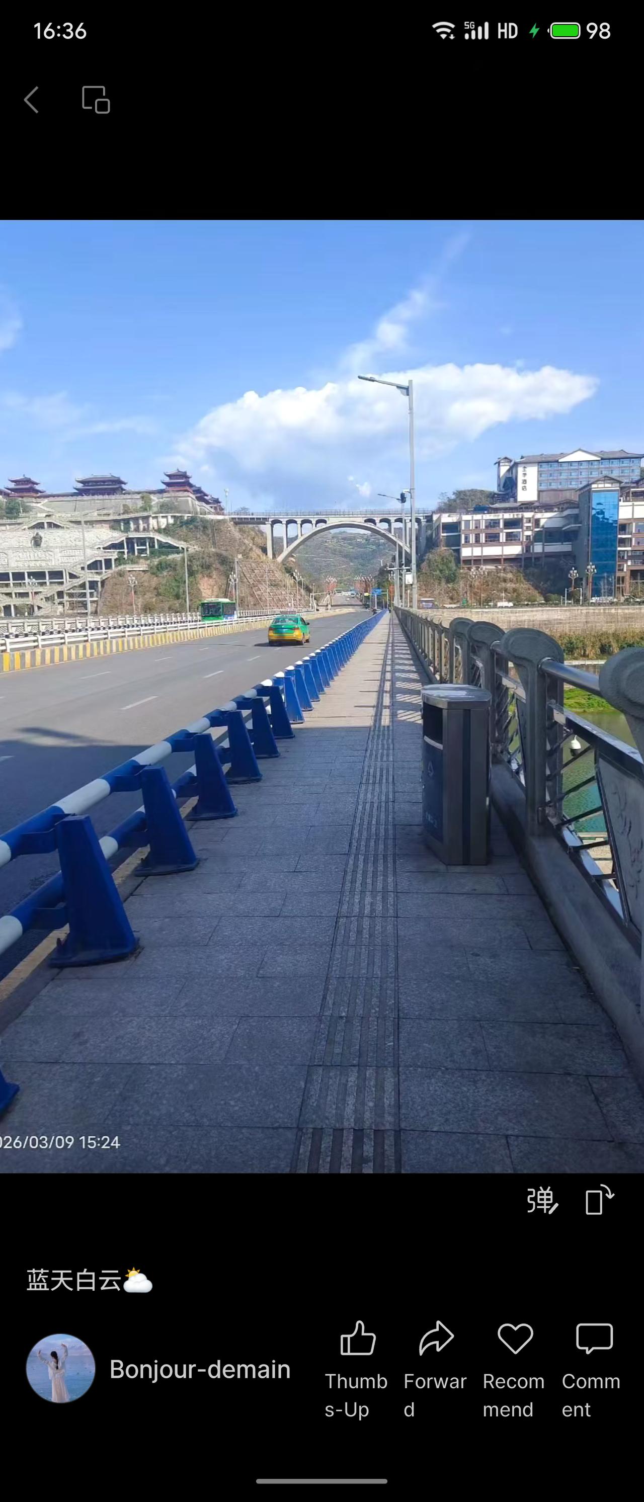 晒图笔记大赛春日桥景，蓝天缀云，车流驰过桥面。蓝白护栏整齐排列，远处古建错落山间