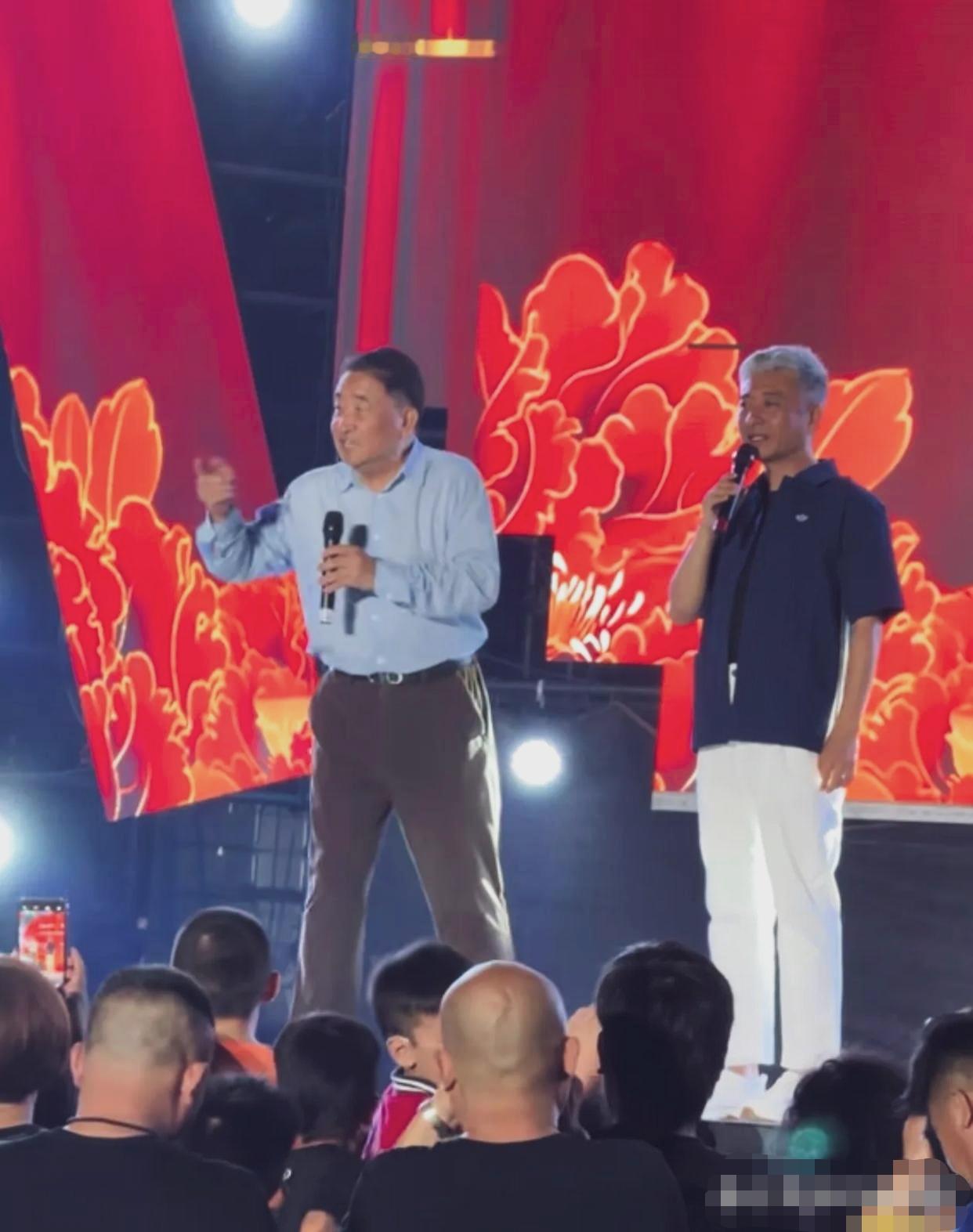 姜昆周炜同台，基层惠民演出现场实拍。
姜昆，浅蓝色衬衫配深色长裤，手握话筒，神情