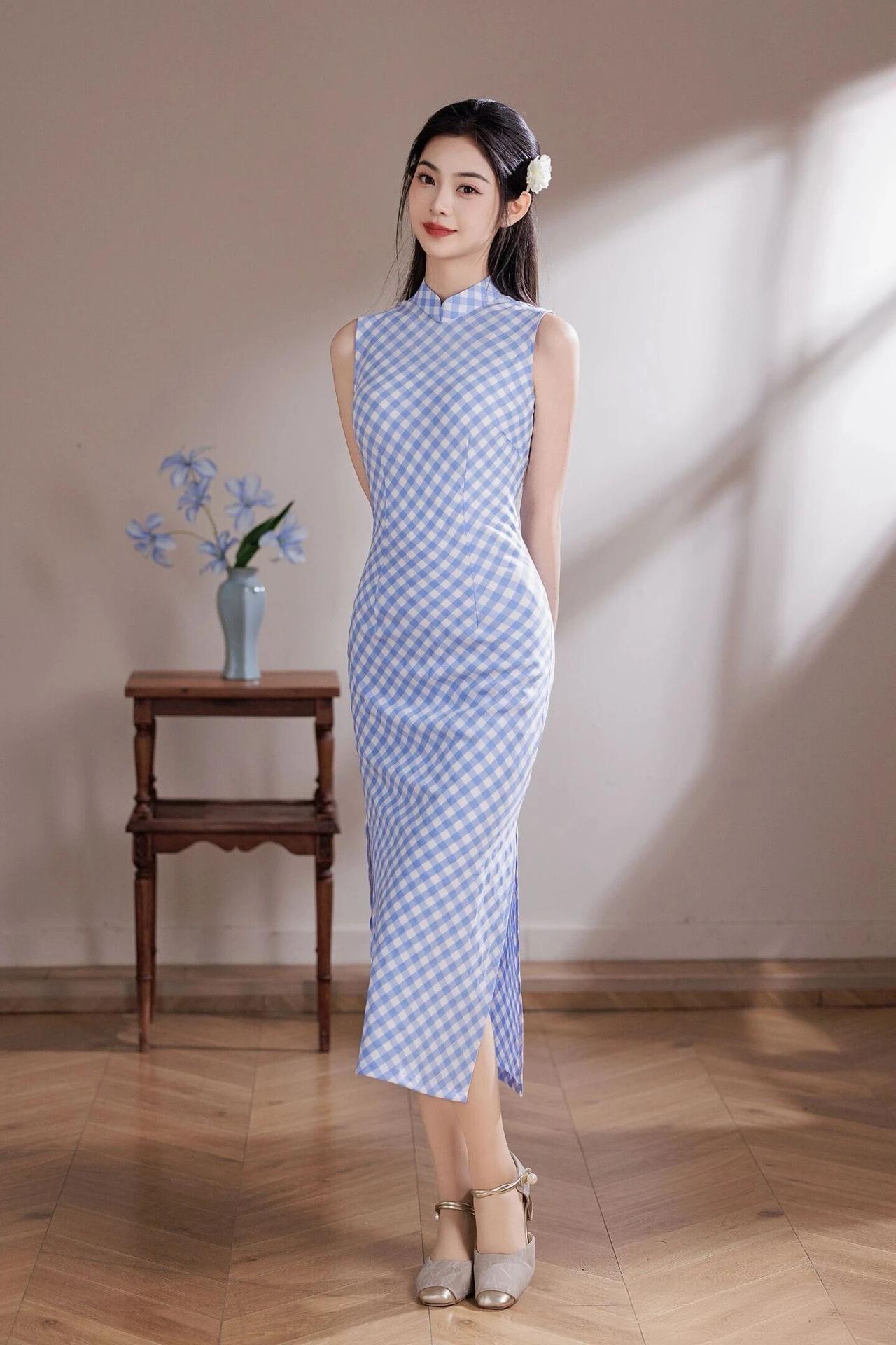 她乌黑长发束起，鬓边别一朵白色小花，温婉又灵动。旗袍采用经典的蓝白格纹面料，清新