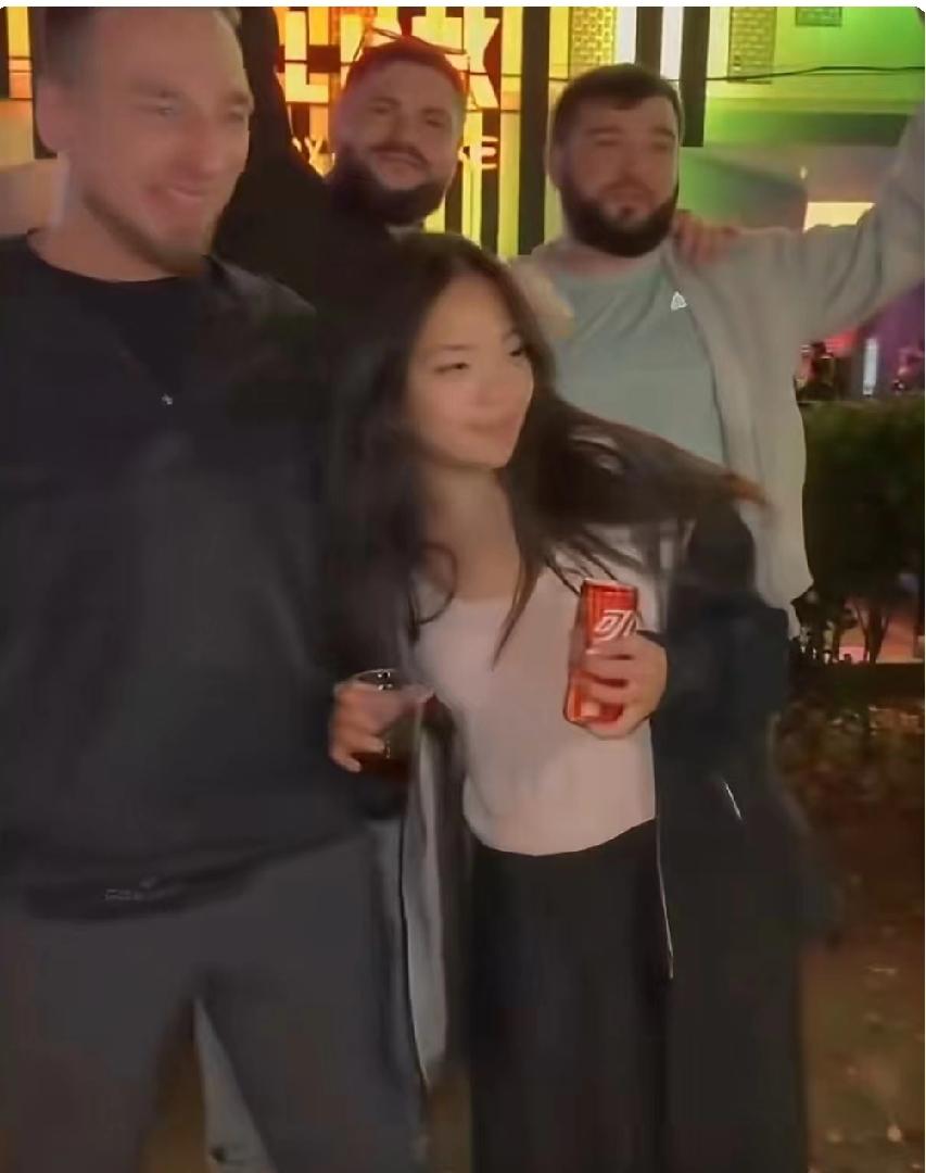 一夜店门口，一名年轻女子和三名外籍男子合影留念时，手持酒水主动往身旁外籍男子身上