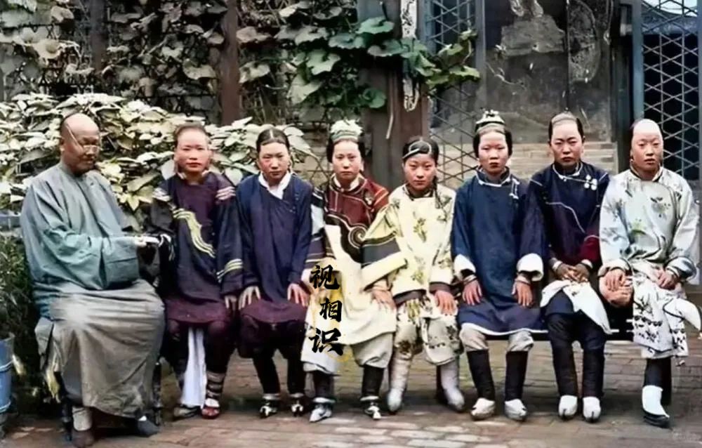 清末时期，一个有钱家老爷与七位妻妾，在自家庭院中的合影照片，镜头中可以看到她们都...