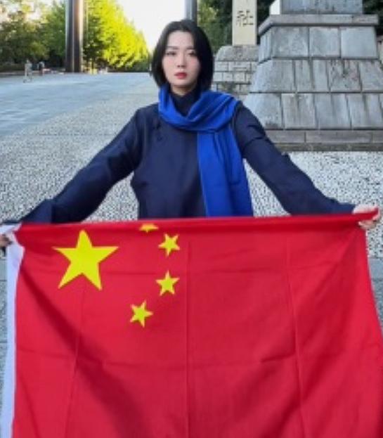 2023年，日本靖国神社前，一名中国女子双臂展开，高举五星红旗，面对周围复杂的目