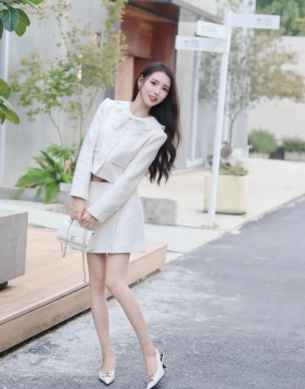 身着米白色粗花呢短款外套与同色系A字短裙，领口饰有荷叶边，整体风格优雅知性。她搭