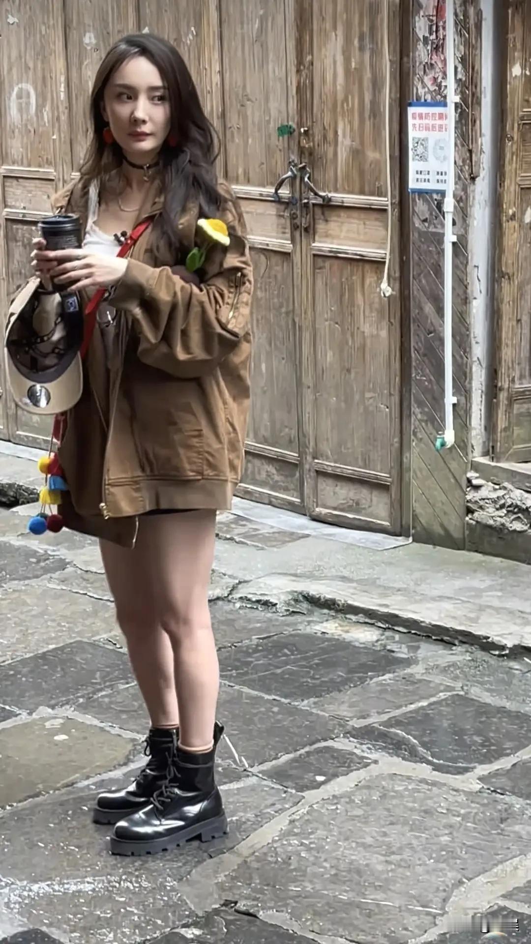 杨幂身着棕褐外套，手持咖啡，在古巷里