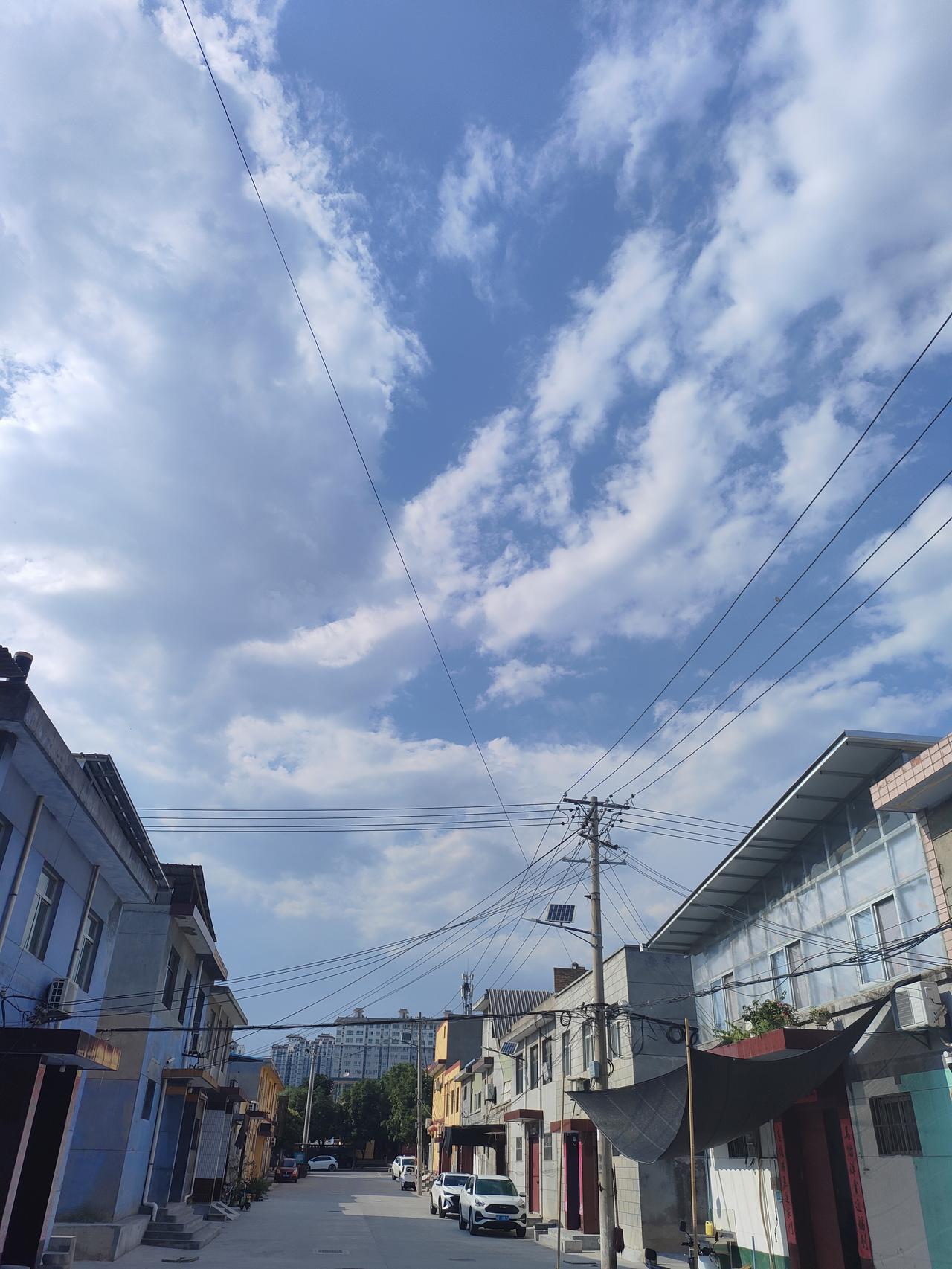 可以分享一张你拍的天空美照吗窄巷两边错落屋舍，电线纵横交错，抬头是澄澈蓝天，蓬松