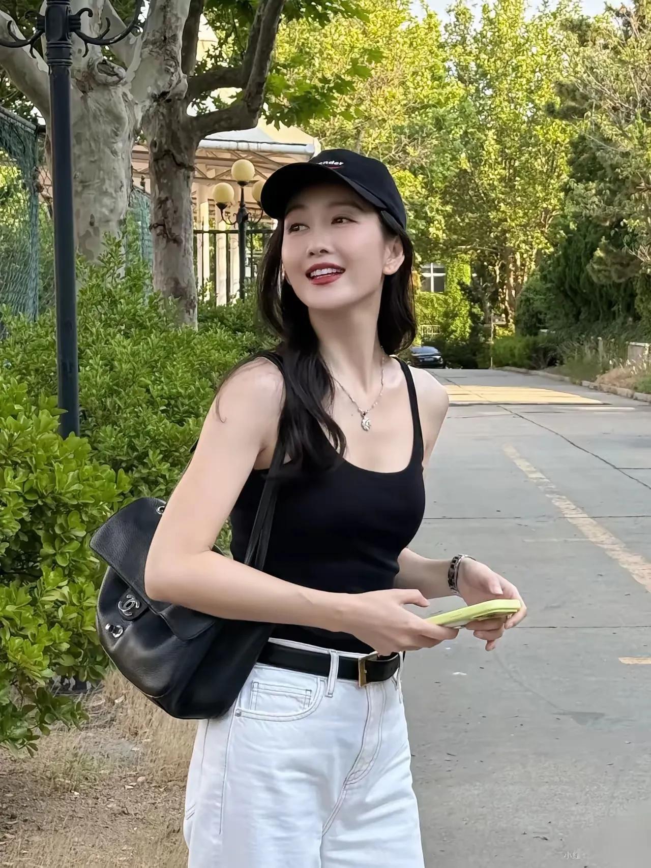 王鸥街头随拍，黑U领吊带搭配高腰白牛仔裤，黑白简约配色清爽显瘦，棒球帽搭配长卷发