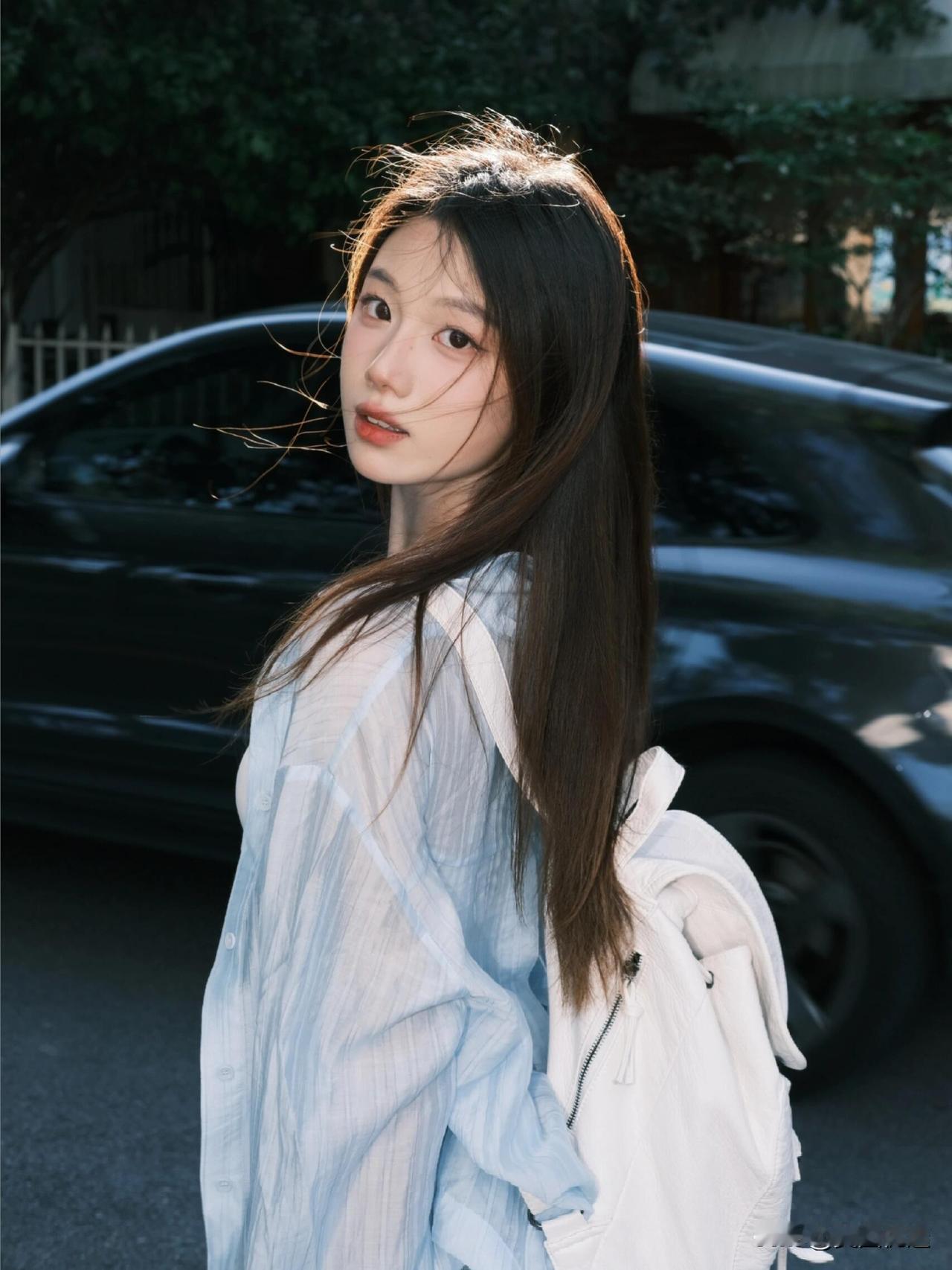 阳光下的温柔少女，背着白色背包，微风轻拂发梢，青春洋溢。
