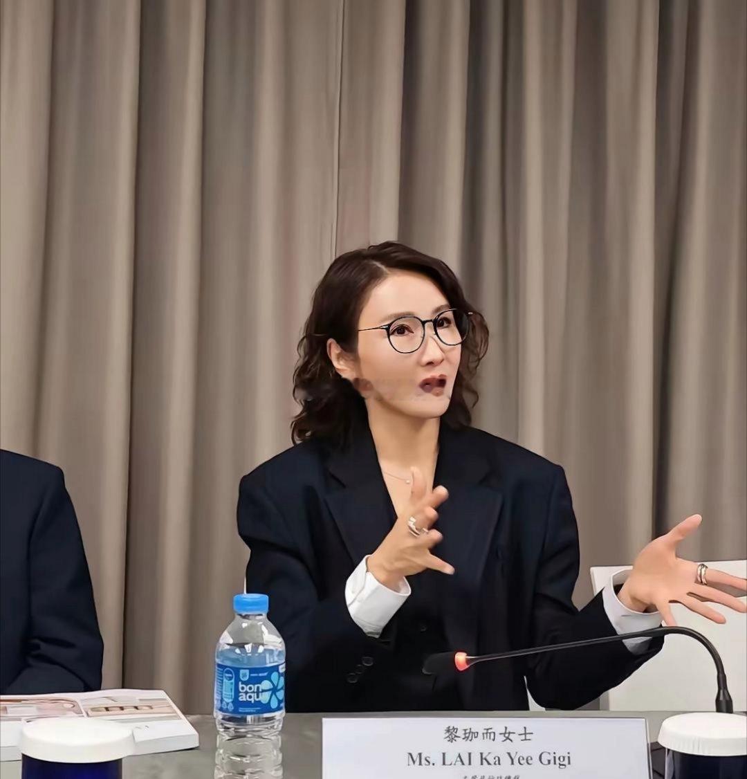 54岁的黎姿以集团主席兼总裁的身份出席股东大会！她穿着黑色西装带着黑框眼镜，显得