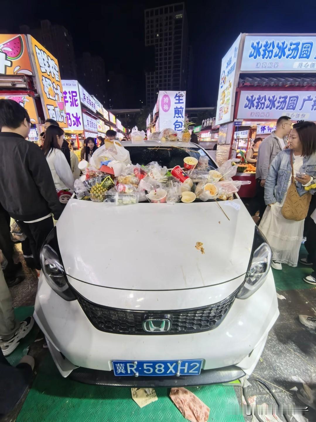 河北石家庄正定夜市，一辆轿车停放在摊位中间，因为挡住了路，车上被来往的顾客随手放