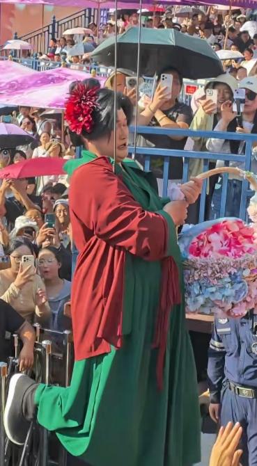 这是年近六旬的大衣哥朱之文，在开封万岁山武侠城男扮女装扮演王婆，吊着威亚撒花瓣，